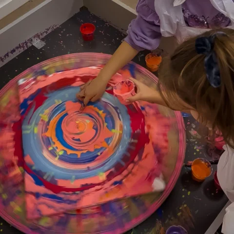 Dziewczynka wylewa farbę na obrotowy stół spin art