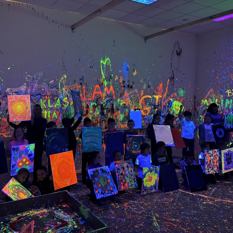 Dzieci pokazują swoje obrazy w sali fluo GlamLama